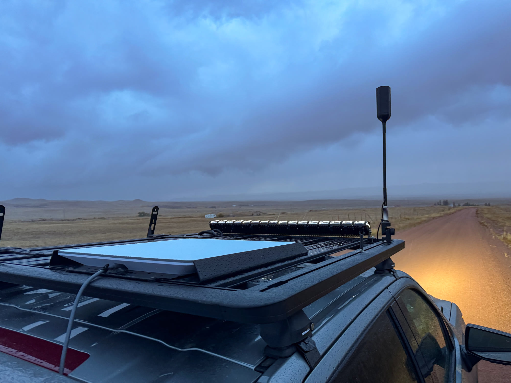 A Starlink flat panel dish mounted on the roof rack of a truck on a rural road